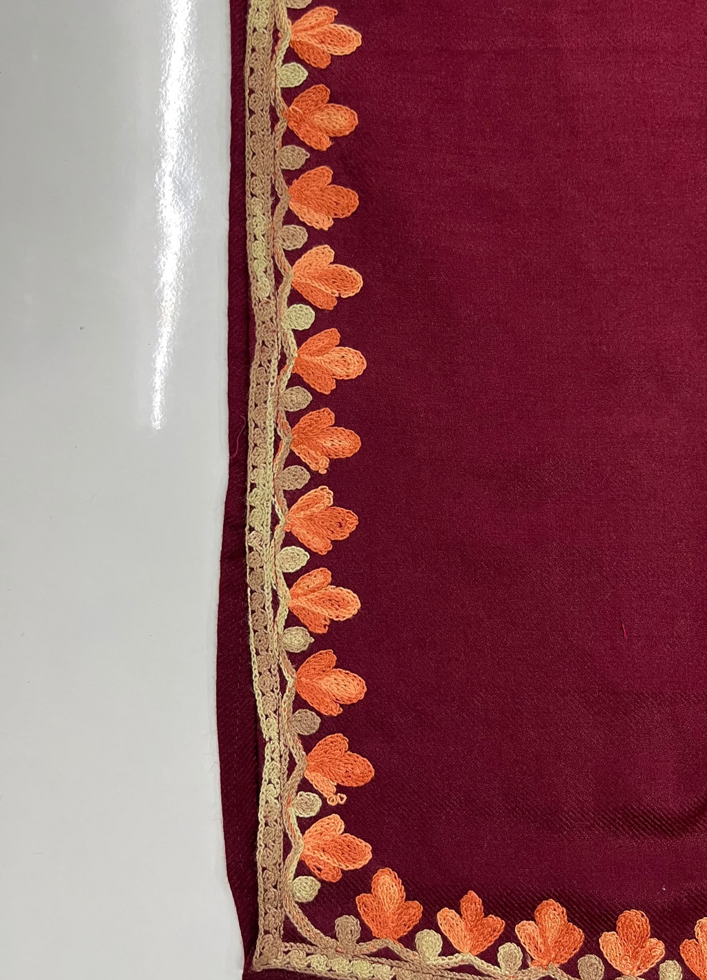 Maroon fabric with orange floral embroidery on a white background
