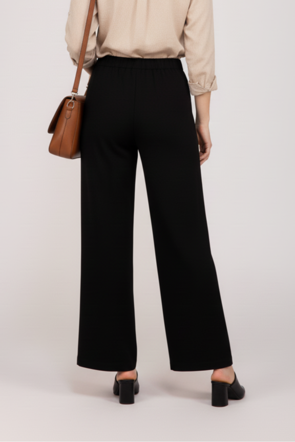 Woman wearing a beige blouse and black wide leg cotton pants with a brown bag on a white background